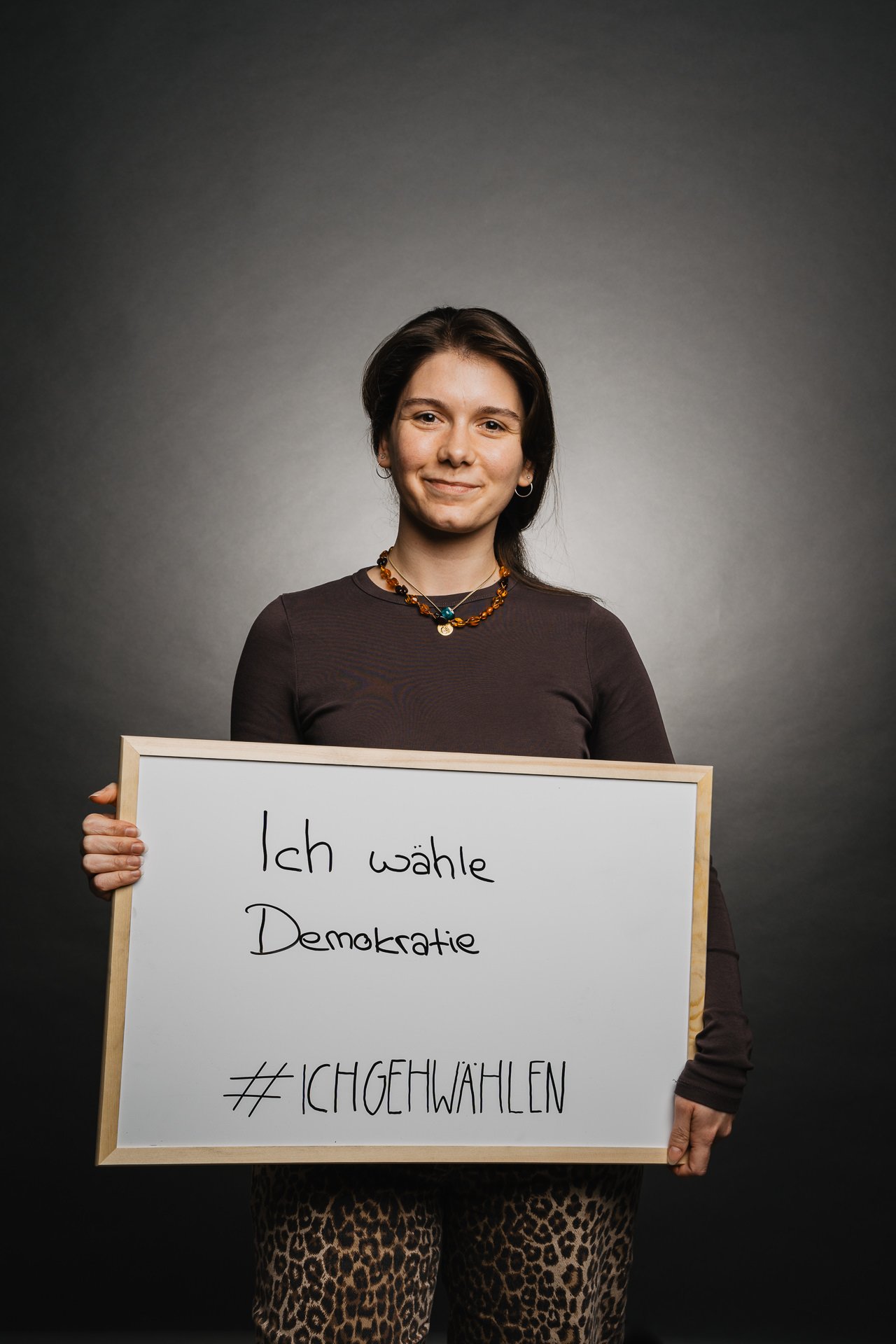Person hält vor dunklem Hintergrund ein Schild mit der Aufschrift „Ich wähle Demokratie“ und „#ICHGEHWAHLEN“.