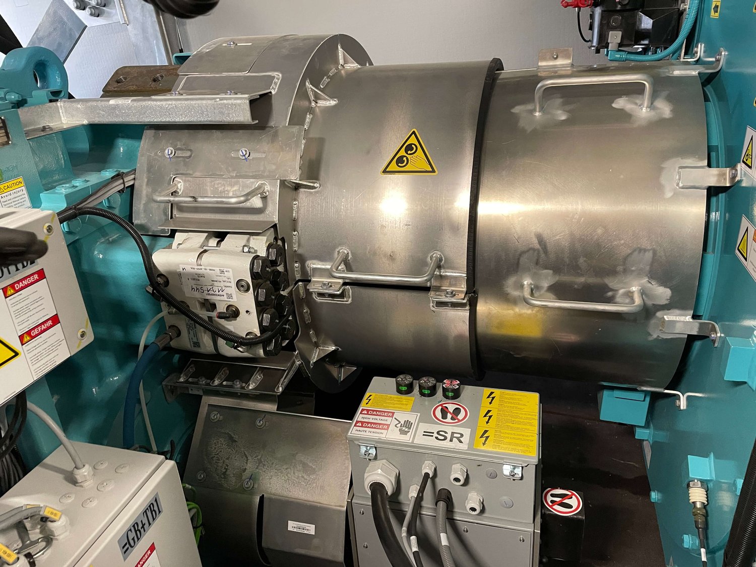 Eine große Industriemaschine mit sichtbaren Metallkomponenten, Sicherheitswarnschildern, elektrischen Leitungen und Bedienfeldern.