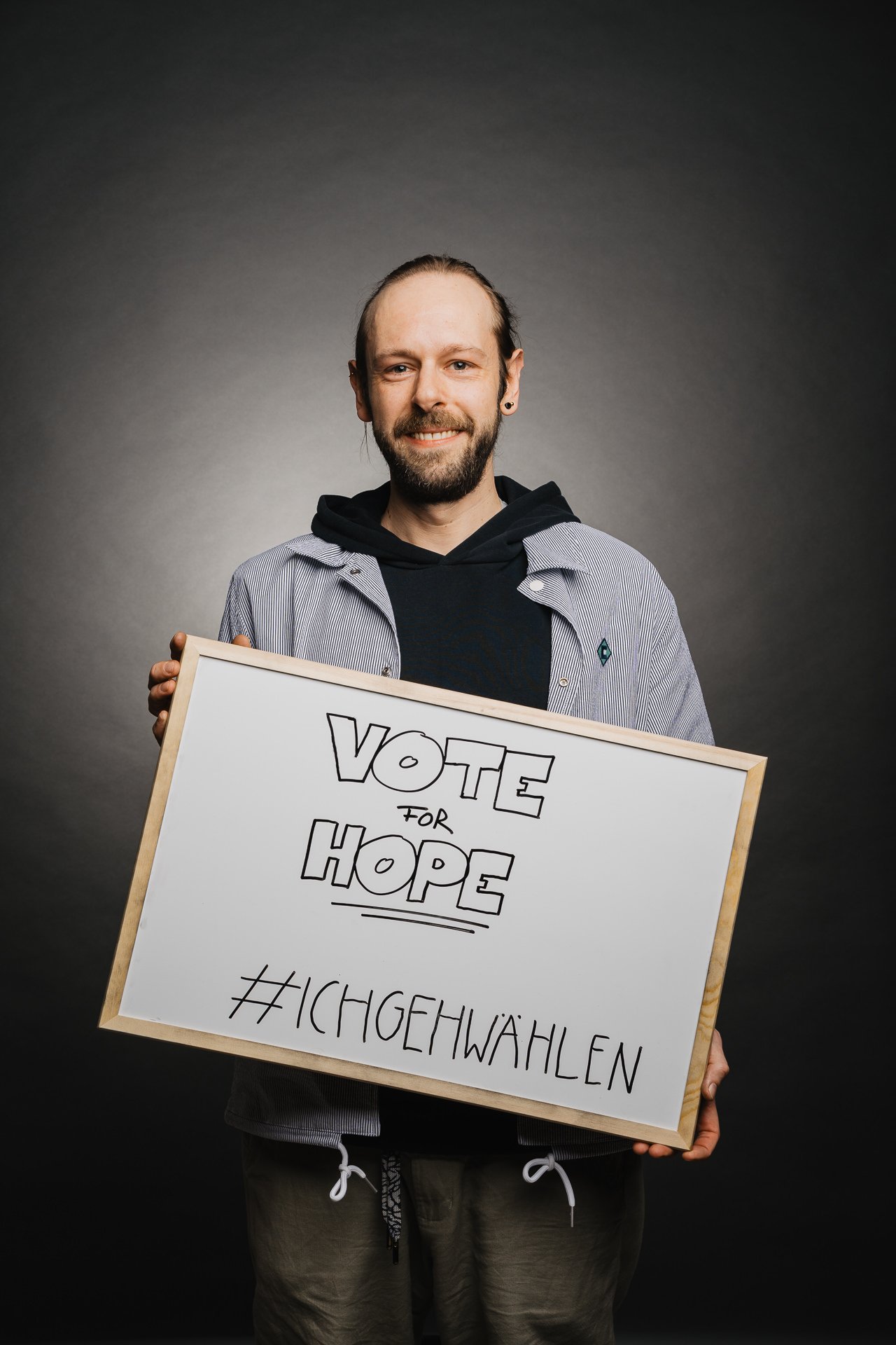 Eine Person hält ein Schild mit der Aufschrift „VOTE FOR HOPE“ und „#ICHGEHWÄHLEN“ vor dunklem Hintergrund.
