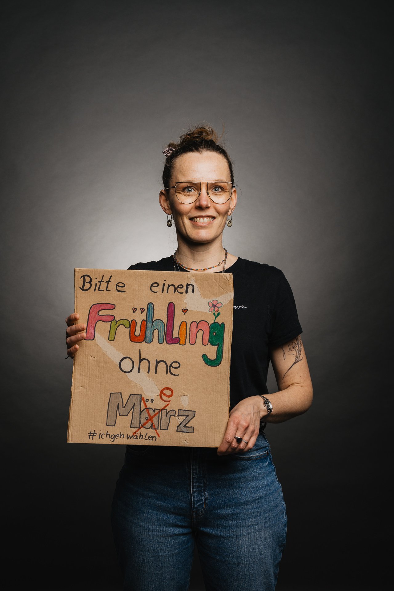 Eine Person hält ein Schild mit der Aufschrift „Bitte einen Frühling ohne März“ in der Hand, mit bunten Buchstaben und kleinen Zeichnungen.