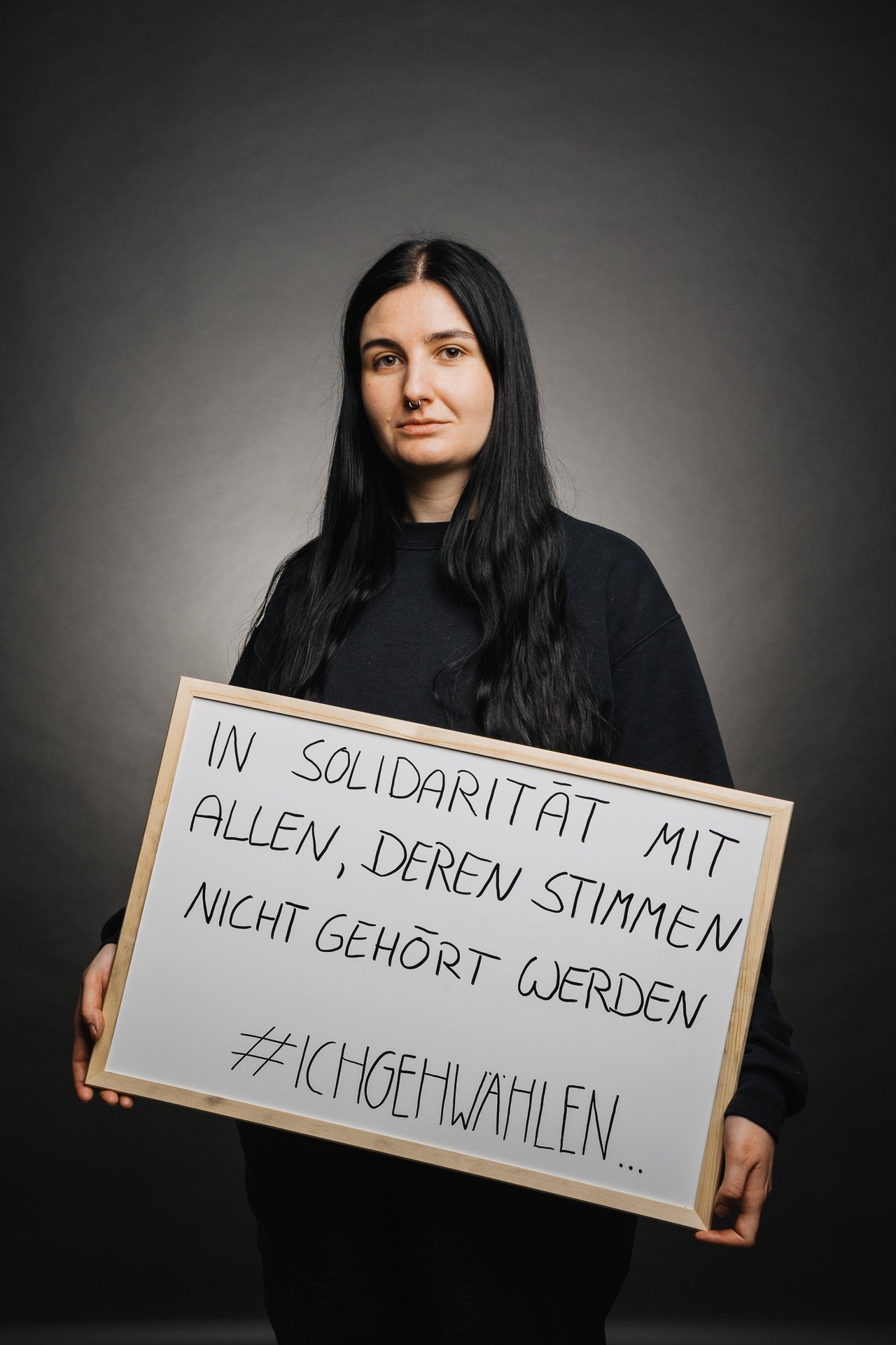 Person, die ein Schild mit einem deutschen Text hält, in dem es darum geht, aus Solidarität mit denen zu wählen, deren Stimme nicht gehört wird.