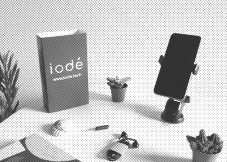 Auf einem Tisch liegen ein Smartphone auf einem Ständer, eine Schachtel mit der Aufschrift „iodé“, kleine Topfpflanzen und Kopfhörer.