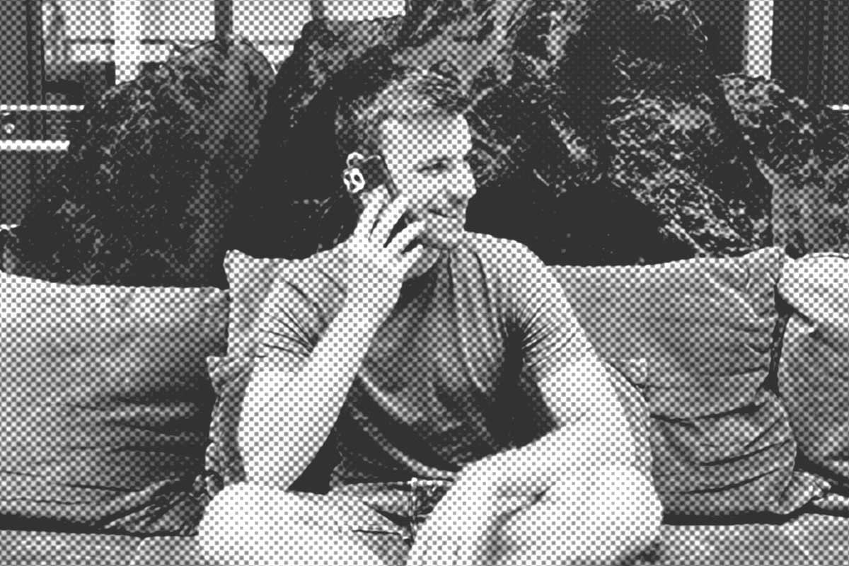 Eine Person sitzt auf einem Sofa und hält ein Telefon ans Ohr. Im Hintergrund sind dunkle Kissen mit Struktur zu sehen.