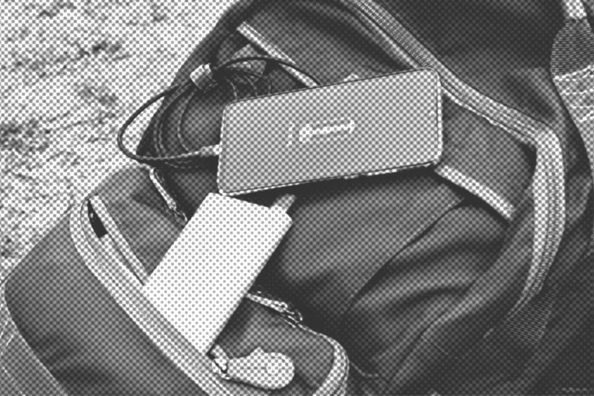 Ein Rucksack mit teilweise geöffneten Reißverschlüssen enthält eine Powerbank und ein tragbares Ladegerät mit Kopfhörern, die auf einer strukturierten Oberfläche liegen.