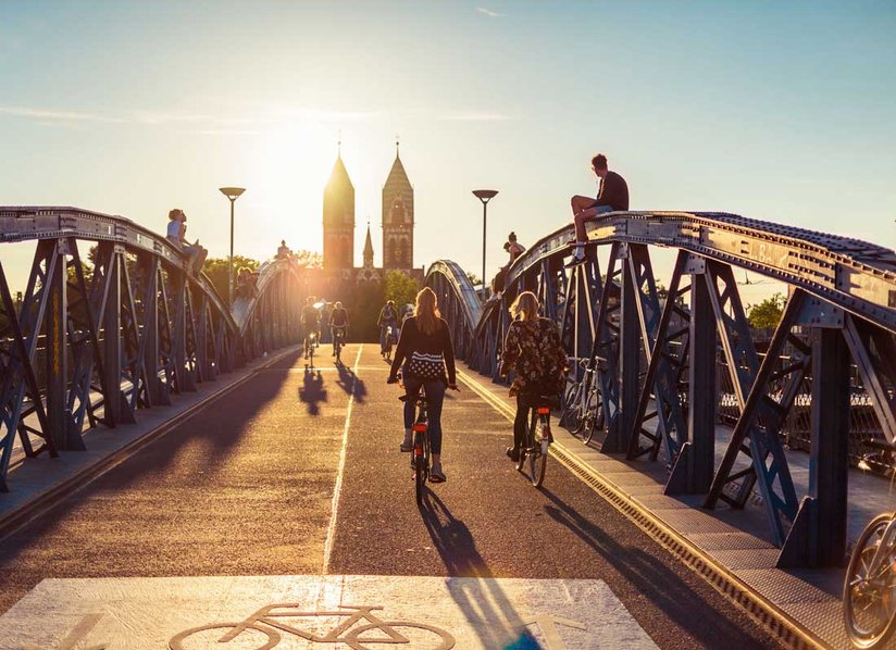 Fahrradfahrer*innen überqueren bei Sonnenuntergang eine Brücke in Freiburg