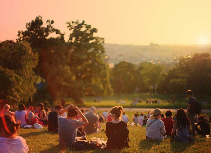 Viele junge Menschen sitzen bei Sonnenuntergang in einem Park auf Wiesenflächen