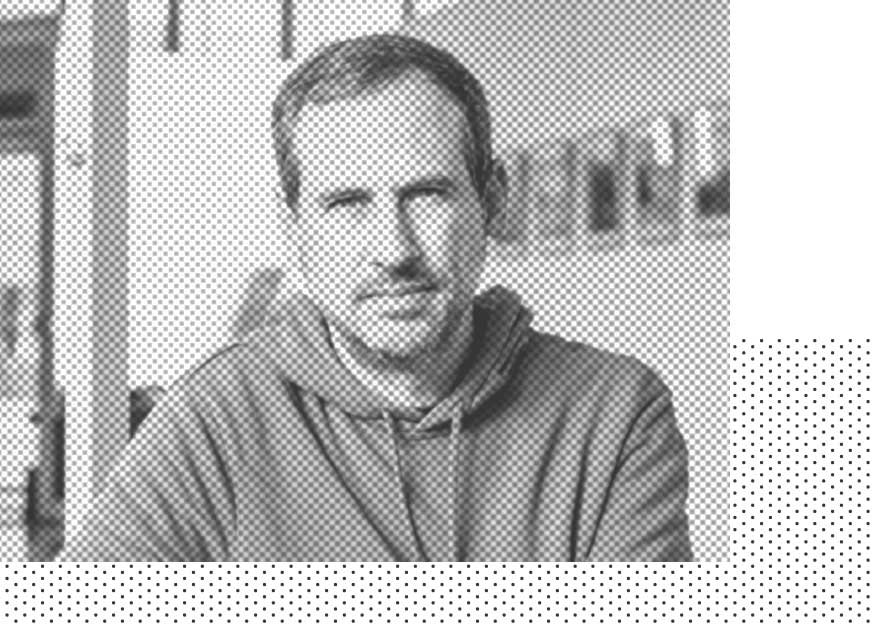 Eine Person in einem Kapuzenpullover blickt in einem Raum mit unscharfen Hintergrunddetails in die Kamera.