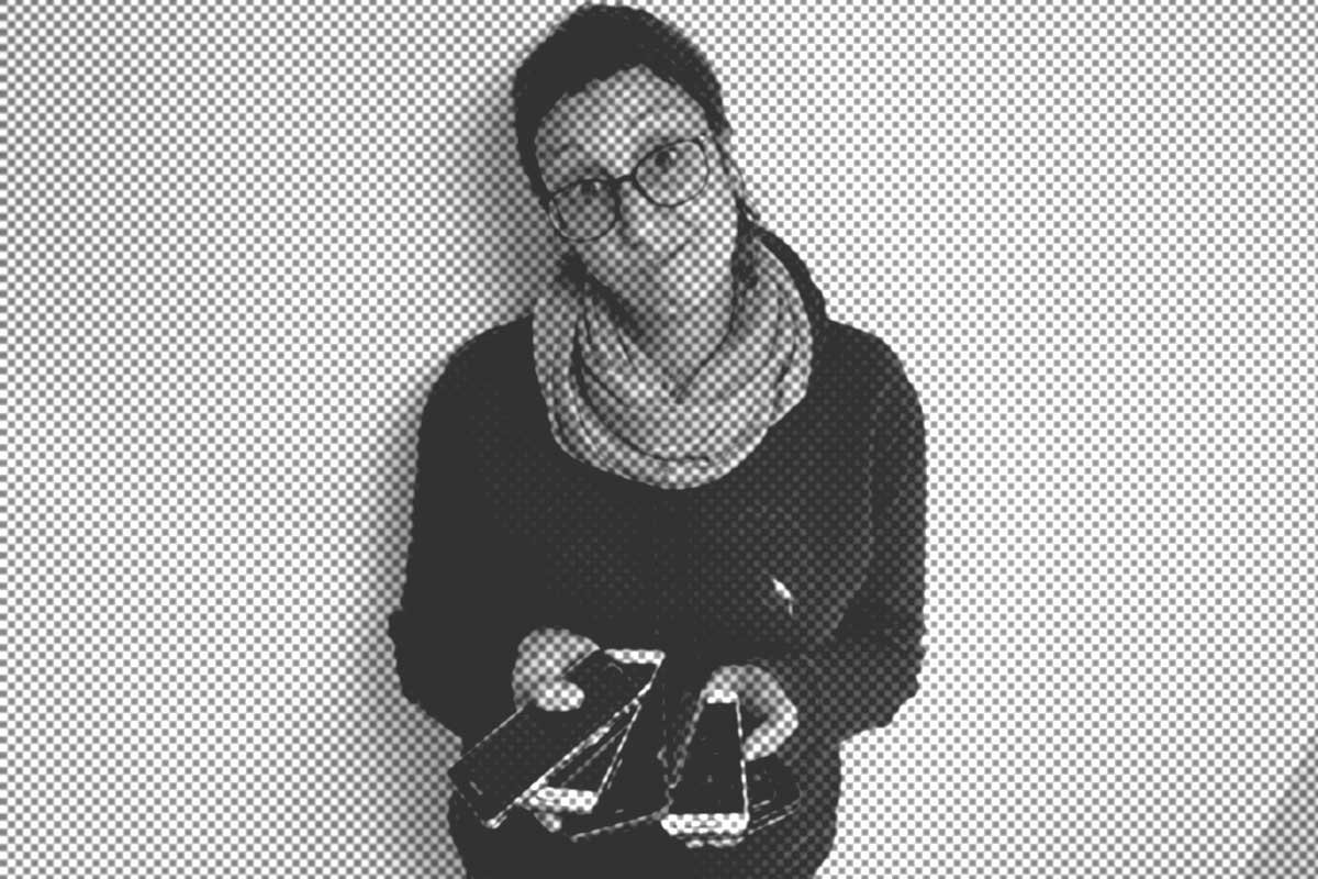 Eine Person mit Brille und Schal hält mehrere Smartphones in den Händen und steht vor einem schlichten Hintergrund.