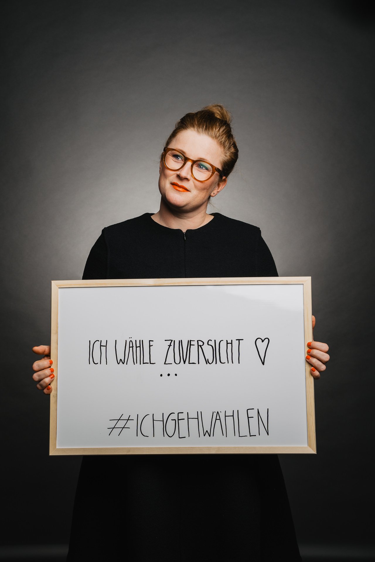 Person hält vor dunklem Hintergrund ein gerahmtes Schild mit der Aufschrift „ICH WÄHLE ZUVERSICHT ♥ ... #ICHGEHWAHLEN“.