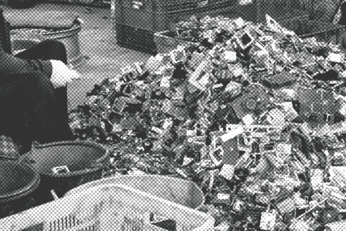 Eine Person steht neben einem großen Haufen Elektroschrott und sortiert in einer Recyclinganlage weggeworfene Geräte.